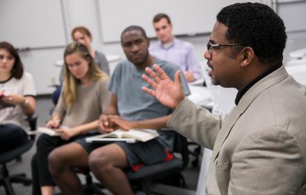 Teacher in front of classroom speaking to students.